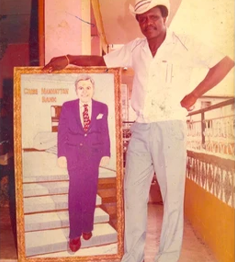 A man in a white shirt and light pants stands indoors next to a large framed portrait print of a suited figure, with the text 'CHINA MANHATTAN BANK' visible on the artwork.